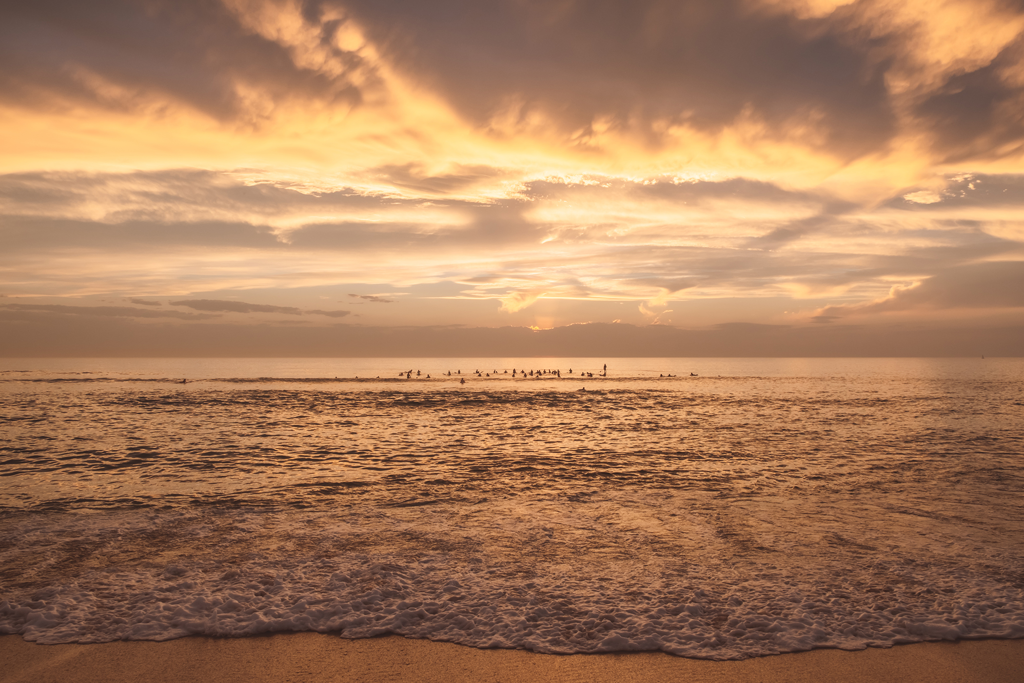 Surfers regardant le soleil se coucher à l'horizon